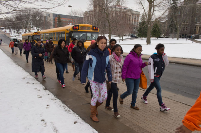 Cultural Excursions: Girls walk down the sidewalk away from a yellow school bus